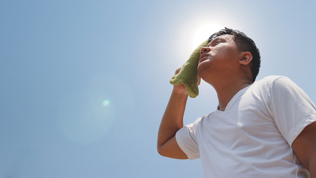 Man wiping sweat off face while standing in the sun.