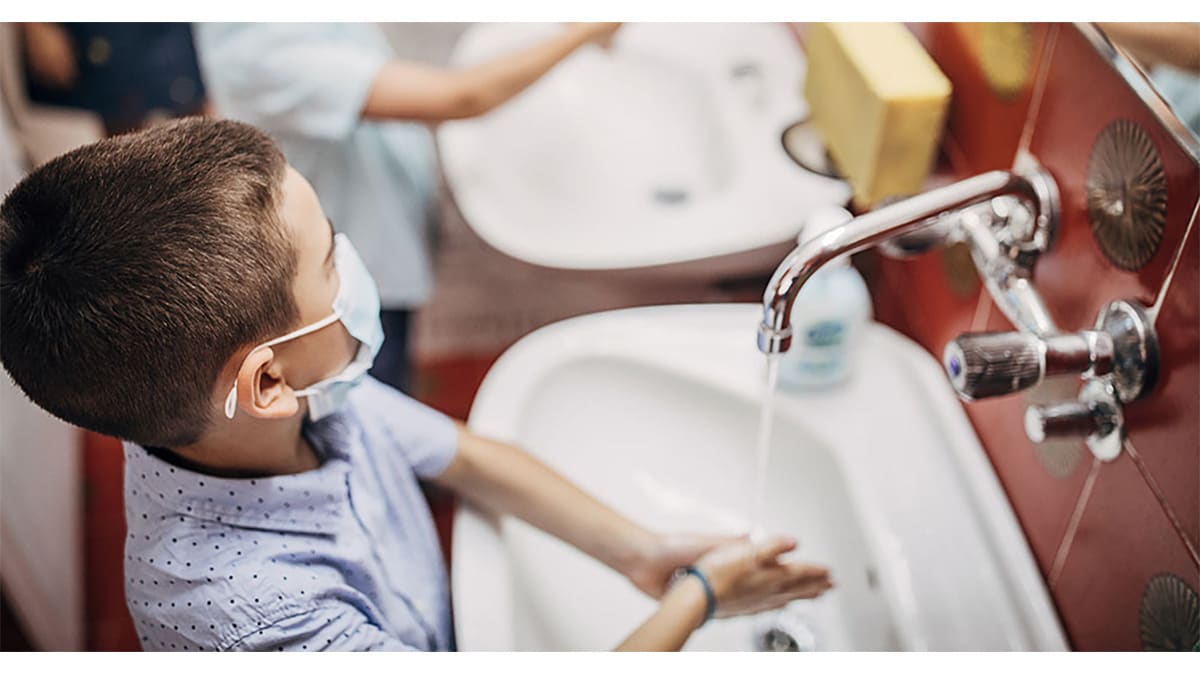 Young boy wearing a mask while washing his hands in the bathroom sink