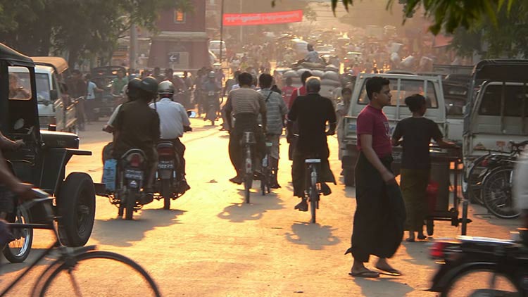 People walking and riding bicycles on a busy street in Mandalay