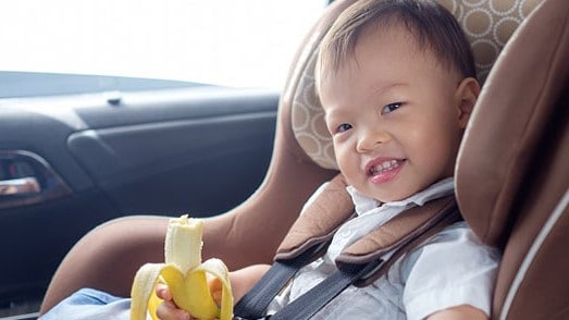 Boy in car seat eating a banana.