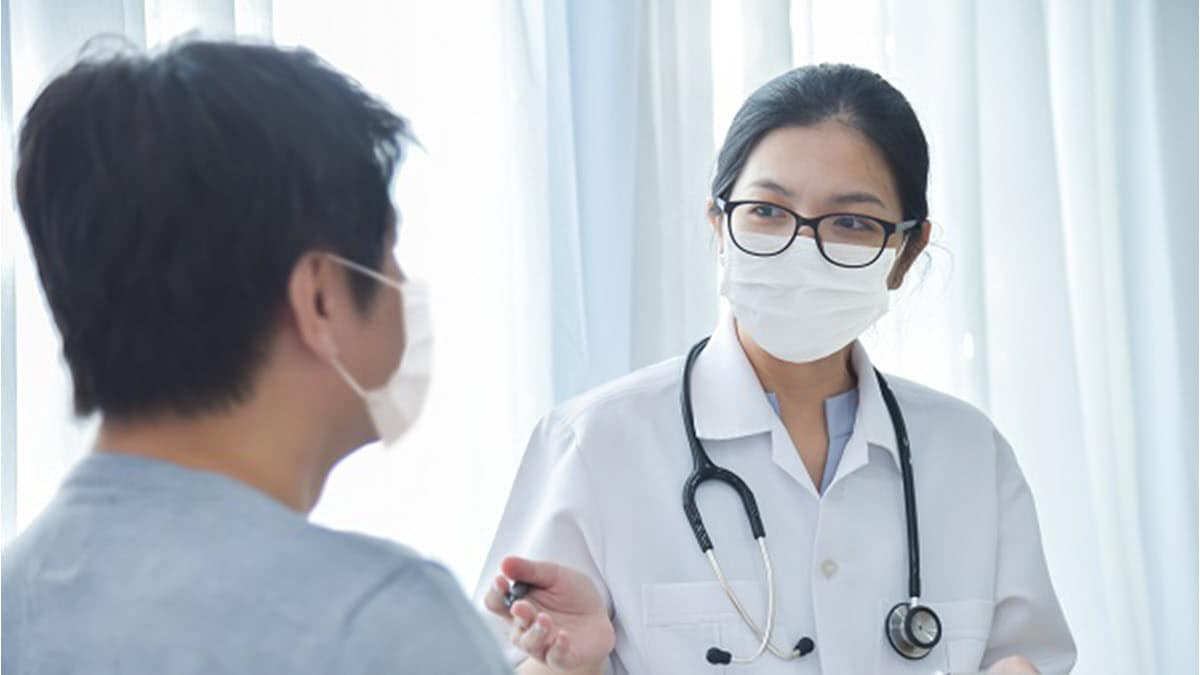 Female doctor talking to a male patient and both are wearing masks