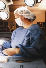 Trabajador de salud que lleva bata completa en un cuarto de operaci%26oacute;n y ayuda con un procedimiento.