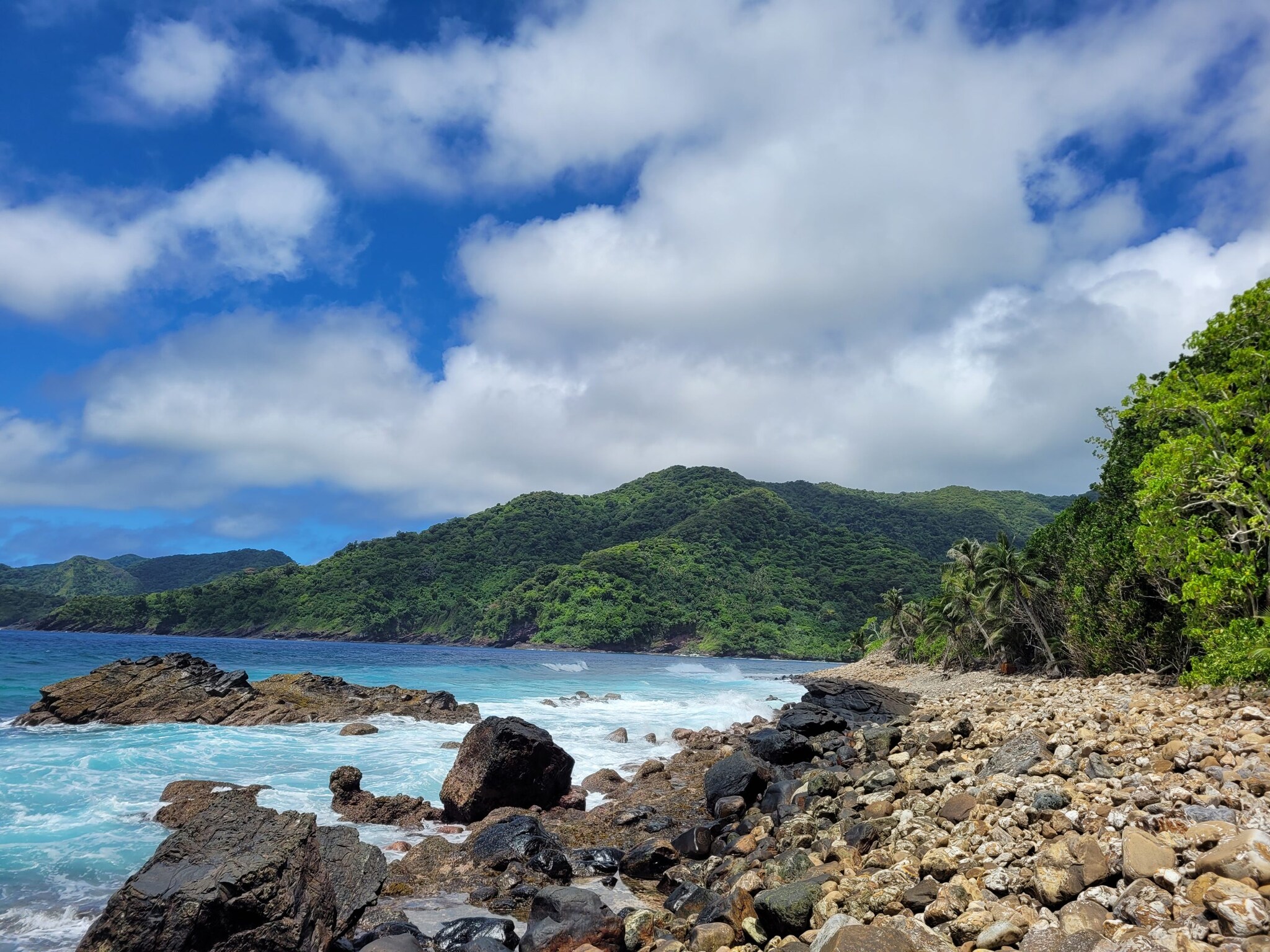 National Park of American Samoa features a rocky beach with a mountainous background.