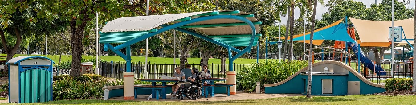 Photo of people enjoying an outdoor picnic under a shade structure near a playground in Australia