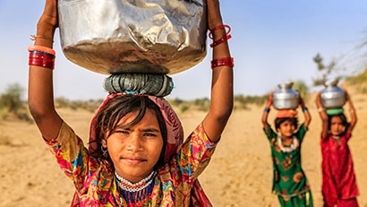 Three young girls carrying containers of water on their heads.
