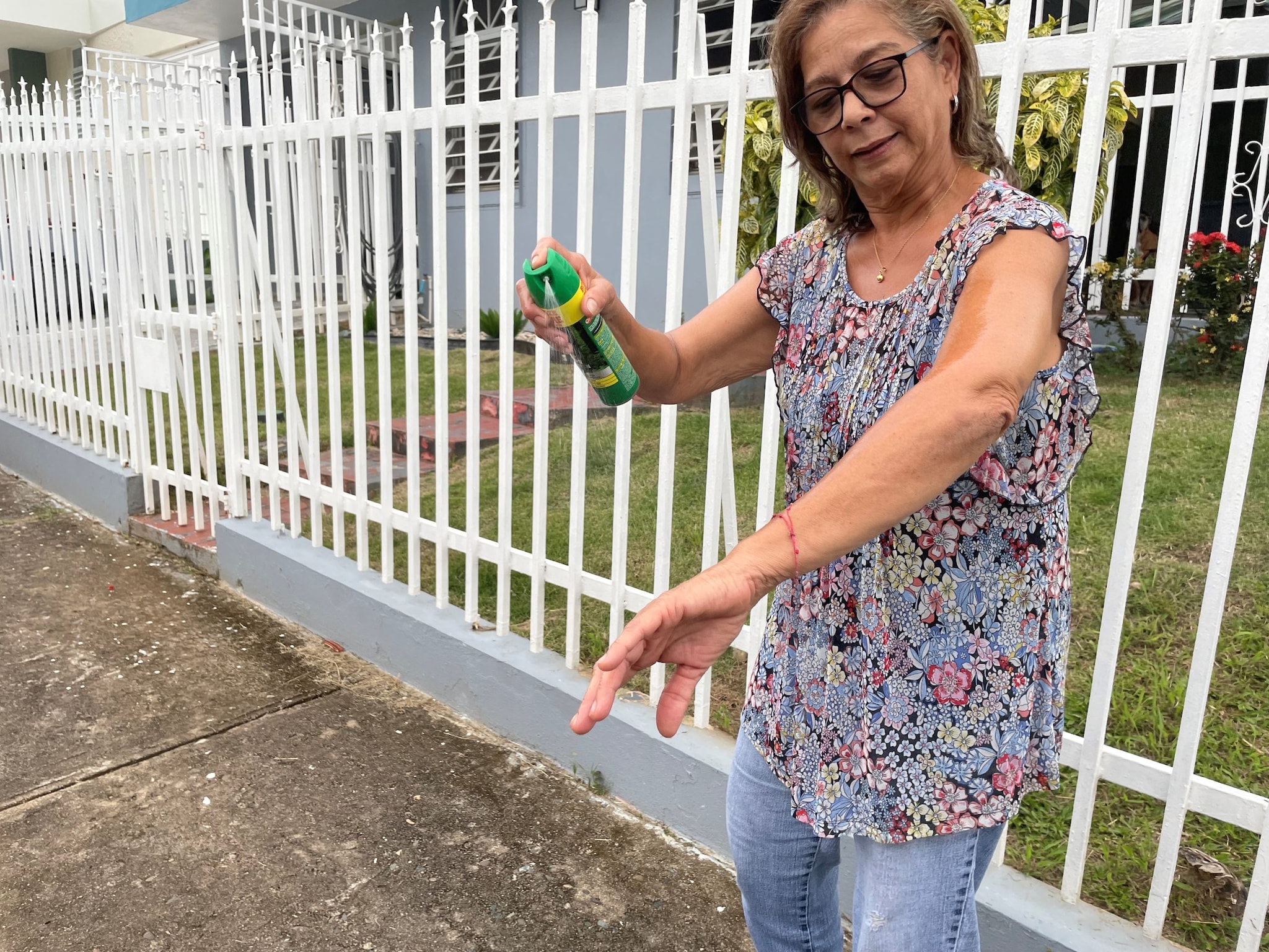 An older woman sprays insect repellent on her arm.