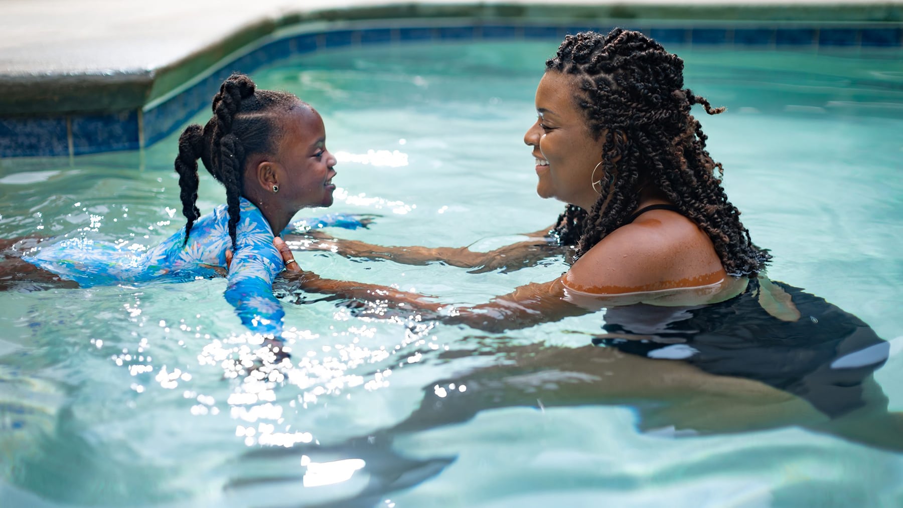 Swim lessons with Black mom and daughter in pool.