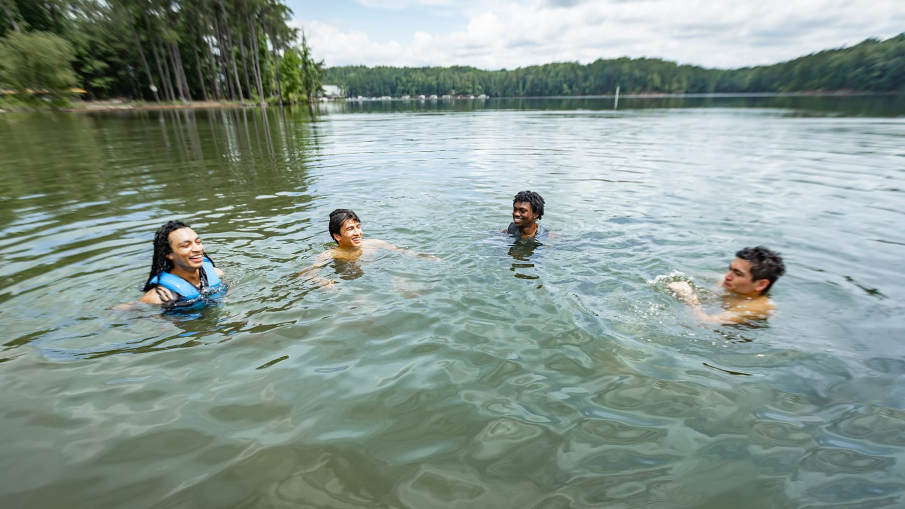 Young men swimming safely together in a lake. Some have life jackets on.