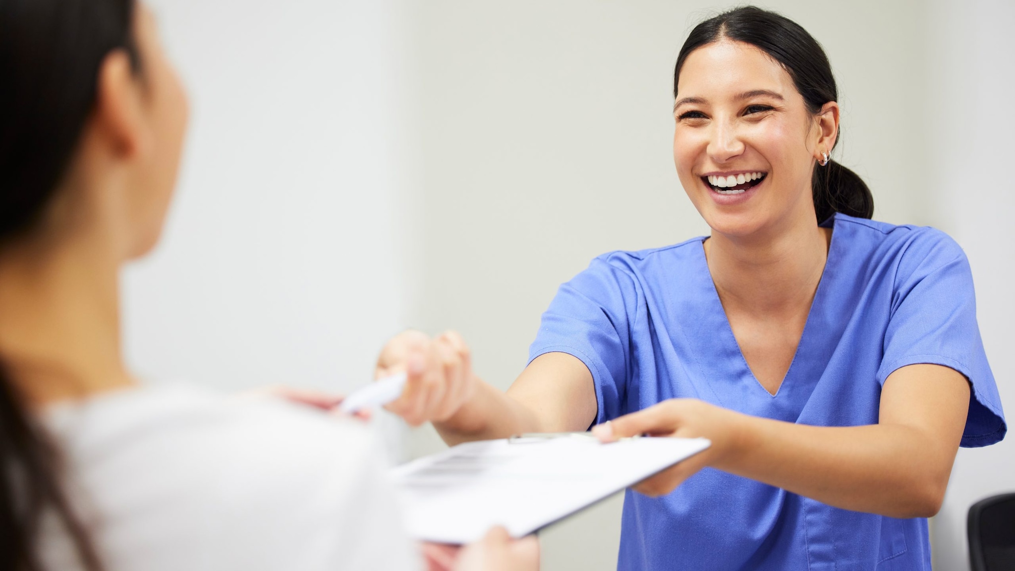 smiling woman wearing blue scrubs passing a piece of paper to another person