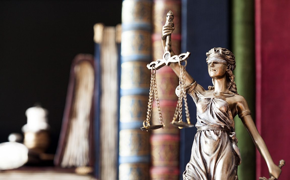 Lady justice statue holding scales with books in the background