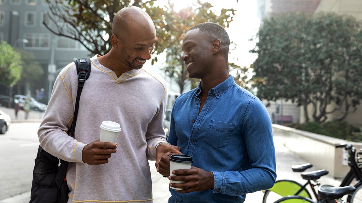 Two men of color smiling and talking outside.