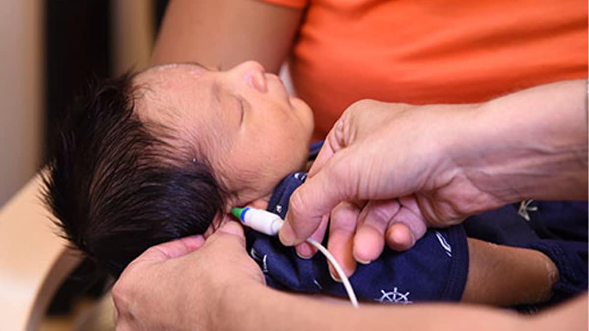 Newborn infant with dark hair is asleep while getting a hearing screen