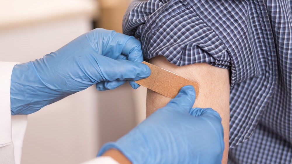 Healthcare professional placing band aid on person's arm following a vaccination.