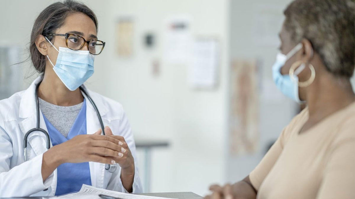 A doctor in a mask talks to an older female patient in a mask.