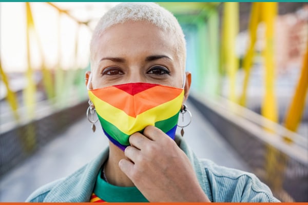 A black woman with very short bleached white hair is wearing a rainbow-colored face mask.