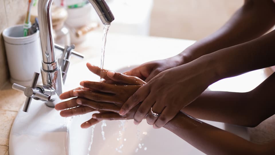 Close-up of black hands under a tap, a mother showing her child how to wash hands properly.