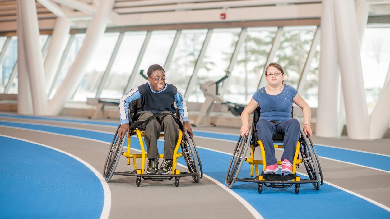 Two teens in wheelchairs moving on a track