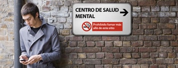 Hombre enviando un mensaje de texto con su celular, afuera de una institución de salud mental