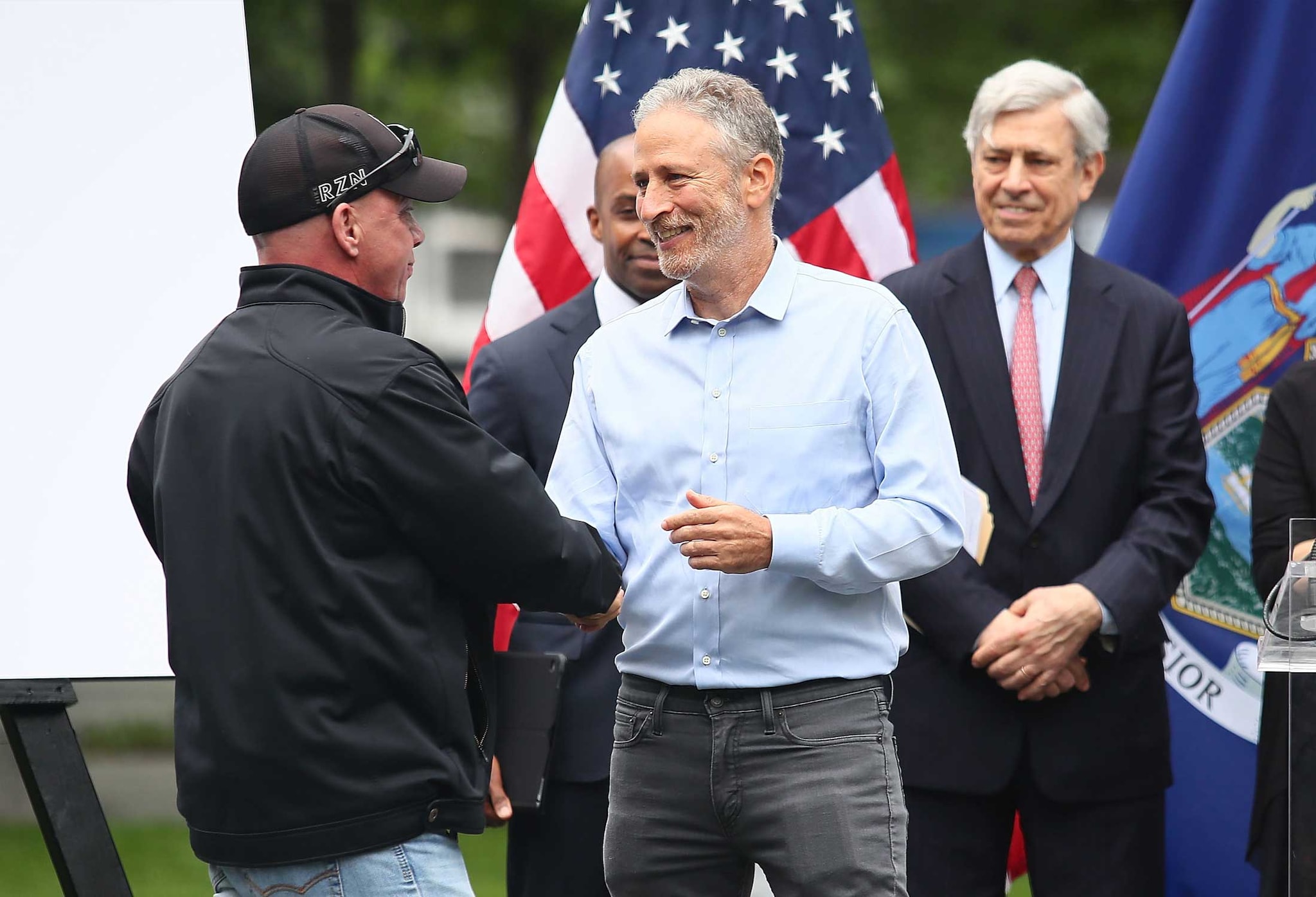 Actor/comedian Jon Stewart (right) greets John Feal (left), the founder of the FealGood Foundation, during the design unveiling of a memorial to honor 9/11 rescue workers on May 30, 2018, in New York City.