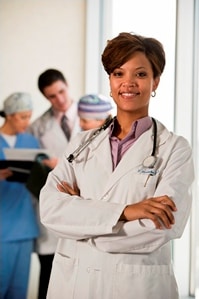 Female doctor smiling at camera with group of doctors looking over a chart in the background