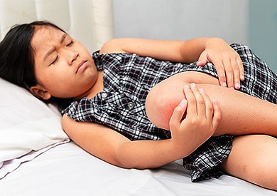 Young girl lying down and holding her painful, arthritic knee.
