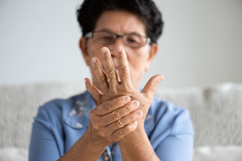 Asian old woman sitting on sofa and having hand pain, hand injury at home. Senior healthcare concept.