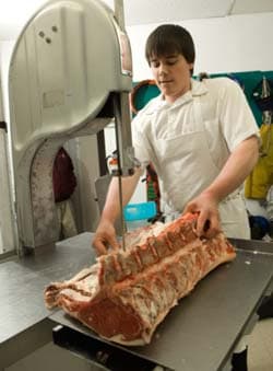 young mad cutting meat on saw