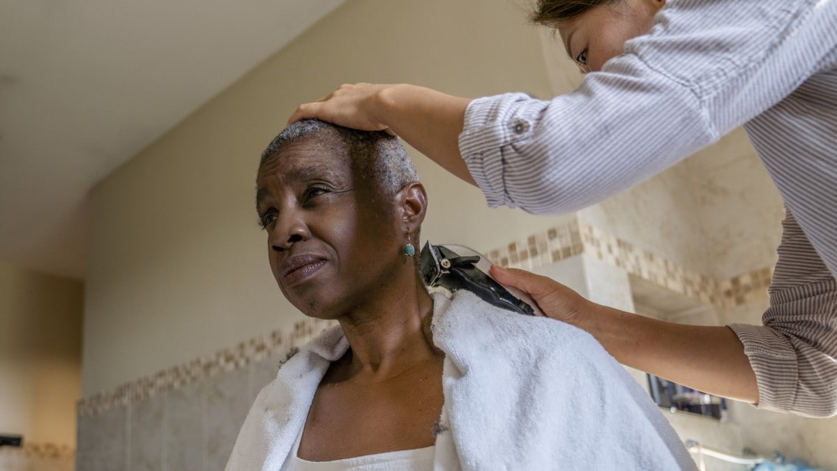 Foto de una mujer afeitando el cabello de una sobreviviente que enfrenta pérdida de cabello