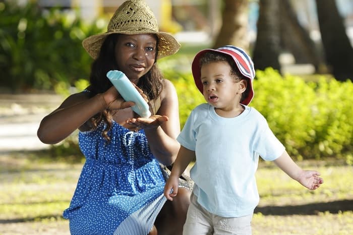 Photo of an African American woman applying sunscreen to her young son
