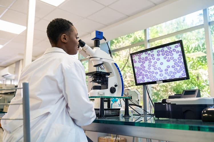 A pathologist looking at a sample under a microscope with the magnified image shown on a computer screen