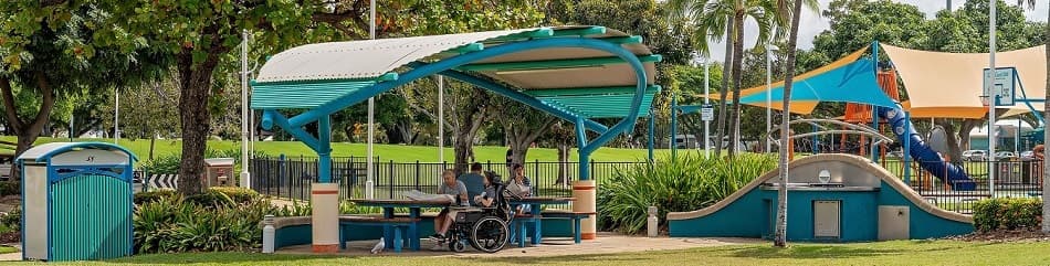 Foto de personas disfrutando de un picnic al aire libre bajo una estructura de sombra cerca de un parque infantil en Australia