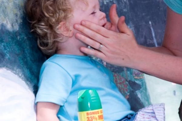 A mother applying insect repellant to a toddler's face with her hands.