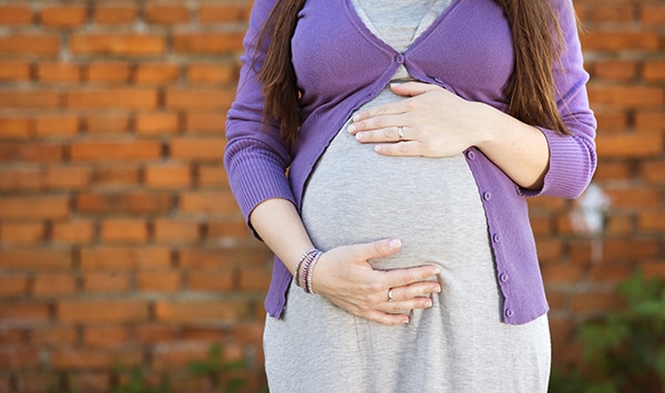 Outdoor portrait of a pregnant woman holding her belly, brick wall in background.