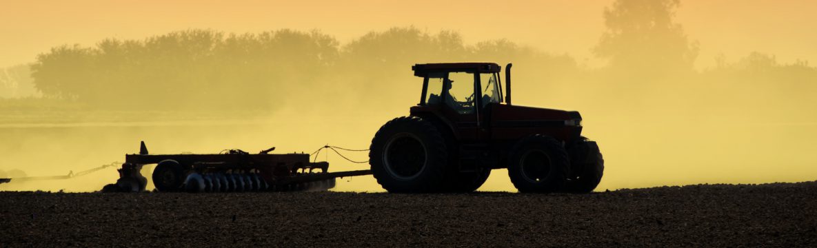Photo of a tractor, silhouetted, in a field, tilling at daybreak.