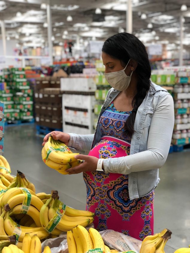 Pregnant woman at the grocery store looking at bananas.