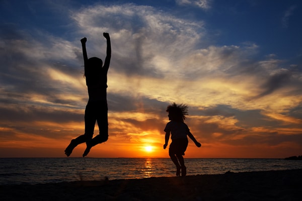 Happy young family have fun on beach and jump at sunset