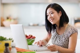 Woman looking at laptop next to a bowl of fruit