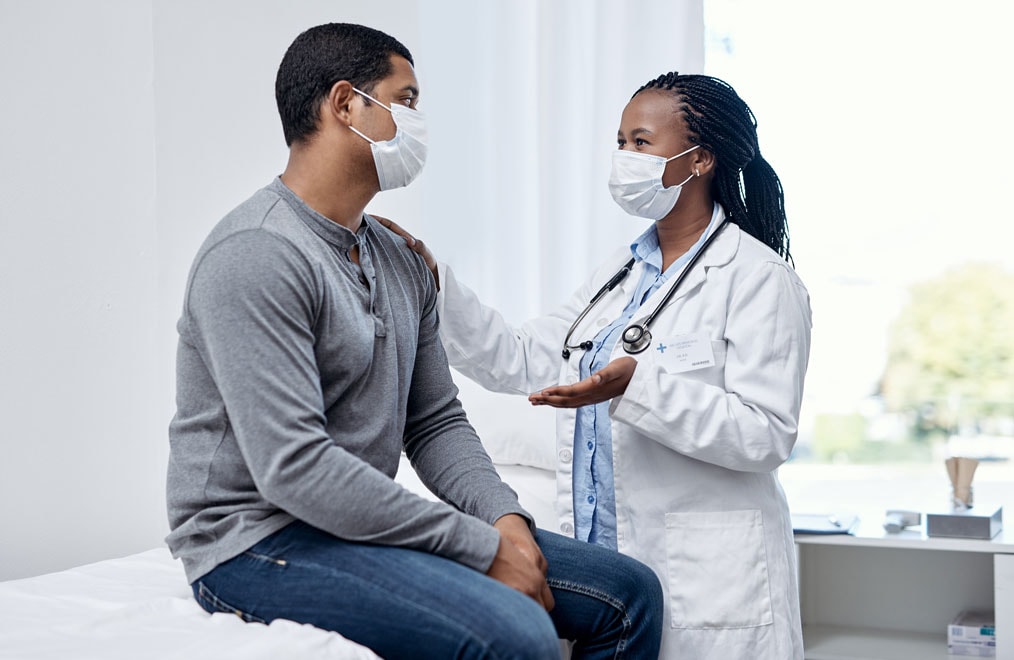 Photo of a female doctor wearing a mask talking to a male patient wearing a mask