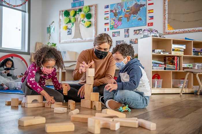 Daycare worker on the floor with children playing with building blocks
