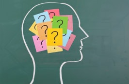 illustration drawn on a blackboard of the profile of a human head with colorful question marks inside it 