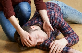 A woman placing an unconscious man in recovery position after a seizure 