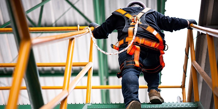 Construction worker wearing a safety harness climbs a staircase
