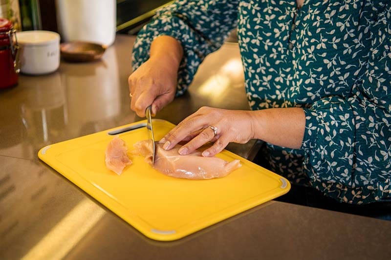 mujer cortando pollo crudo en una tabla de cortar