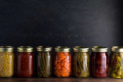 Line of canning jars with various vegetables inside.