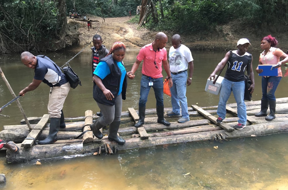 Liberian disease detective trainees carefully cross a river on a long raft to reach remote settlements.