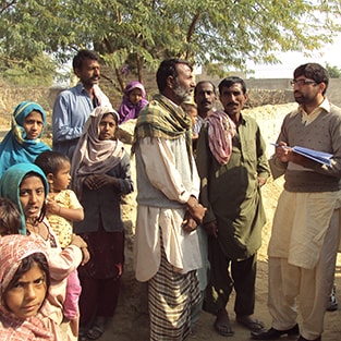 Epidemiologist and villager in discussion in Pakistan, surrounded by children and other men from village.