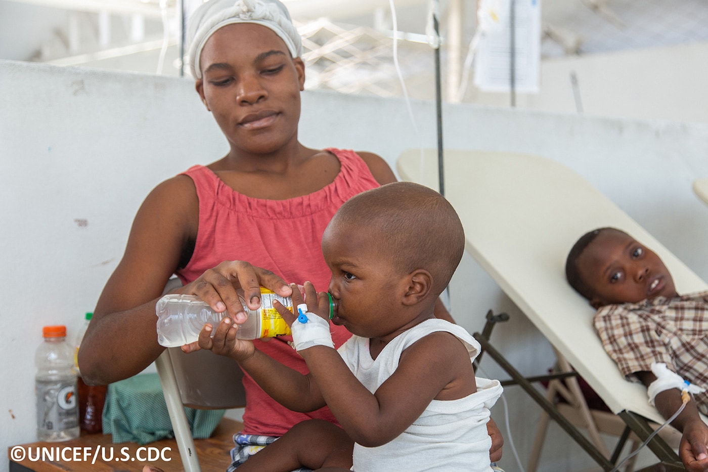 Picture of a child drinking a beverage while sitting on his mother’s lap, during treatment for cholera at a health center.