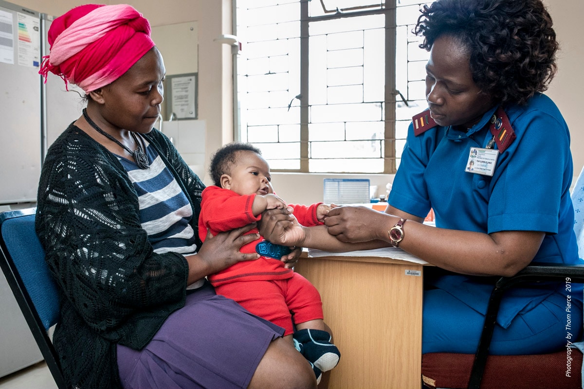 mother comforts baby as healthcare worker examines their hands