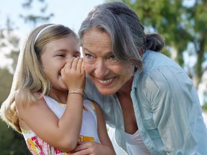 Young girl whispering into elderly women's ear