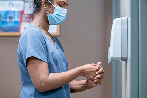 A nurse uses a hand sanitizing dispenser in the clinic